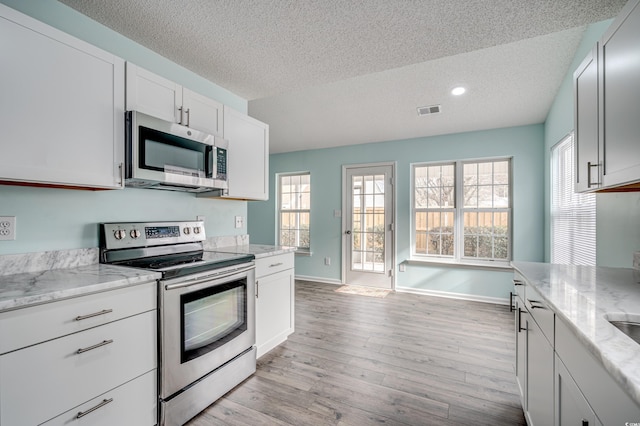 kitchen with light stone countertops, white cabinets, a textured ceiling, and appliances with stainless steel finishes