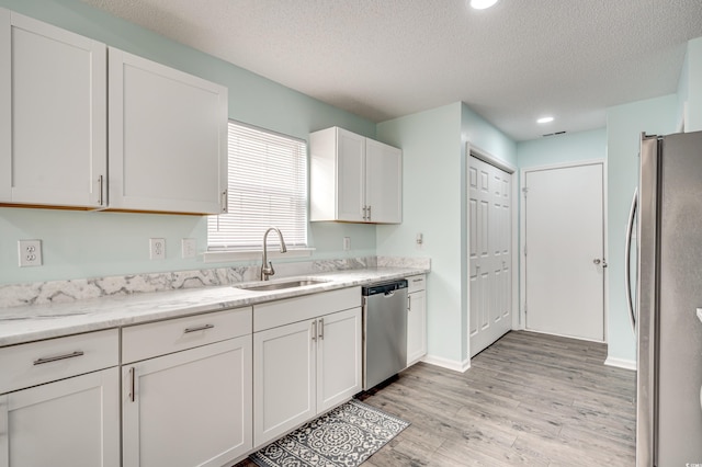 kitchen with appliances with stainless steel finishes, a textured ceiling, white cabinetry, and sink