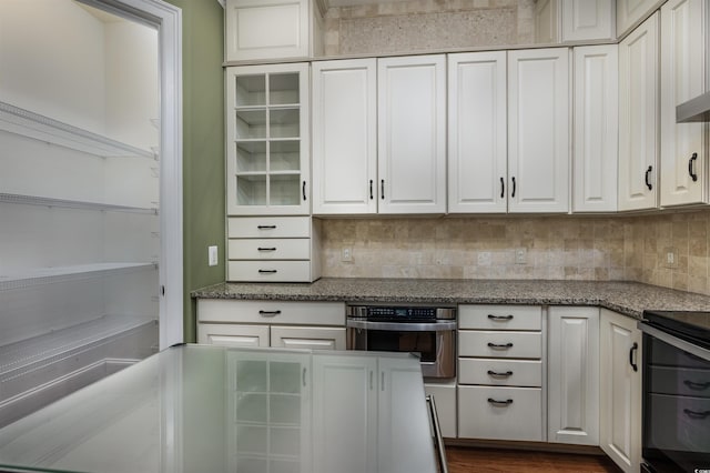 kitchen with white cabinets, oven, backsplash, and dark stone counters