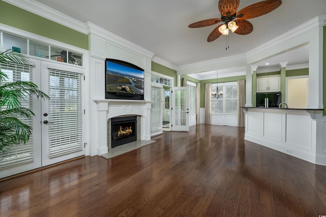 unfurnished living room with french doors, ornamental molding, ceiling fan with notable chandelier, dark wood-type flooring, and a fireplace