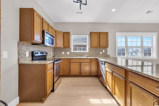 kitchen featuring stainless steel appliances, visible vents, brown cabinetry, a sink, and light stone countertops