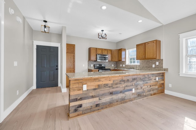 kitchen with vaulted ceiling, decorative backsplash, light hardwood / wood-style floors, kitchen peninsula, and stainless steel appliances