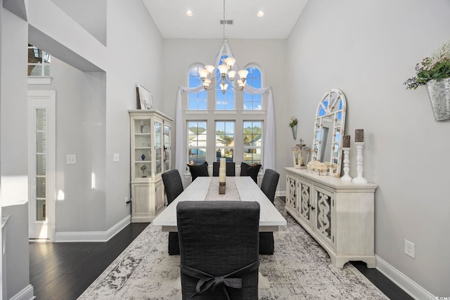 dining area featuring dark hardwood / wood-style flooring, a towering ceiling, and an inviting chandelier