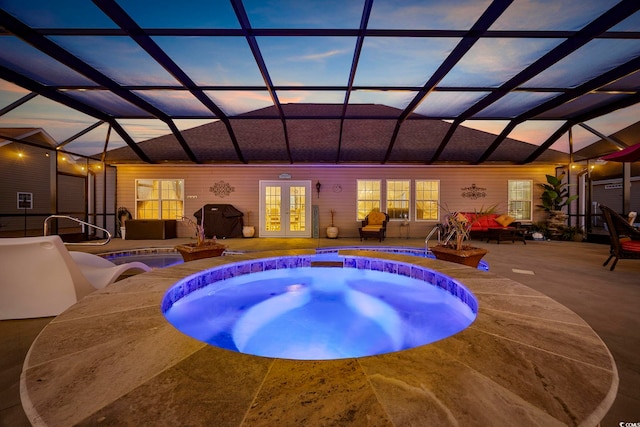 pool at dusk featuring a lanai, an in ground hot tub, french doors, and a patio