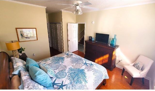 bedroom with hardwood / wood-style flooring, ceiling fan, ornamental molding, and a closet