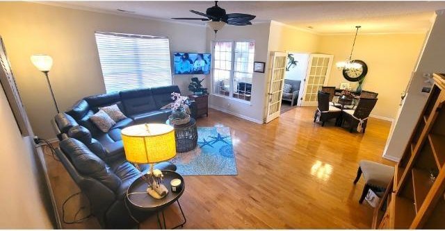 living room featuring crown molding, ceiling fan with notable chandelier, and hardwood / wood-style flooring