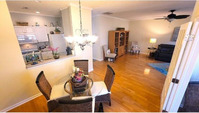 dining area with hardwood / wood-style flooring, ceiling fan with notable chandelier, and ornamental molding