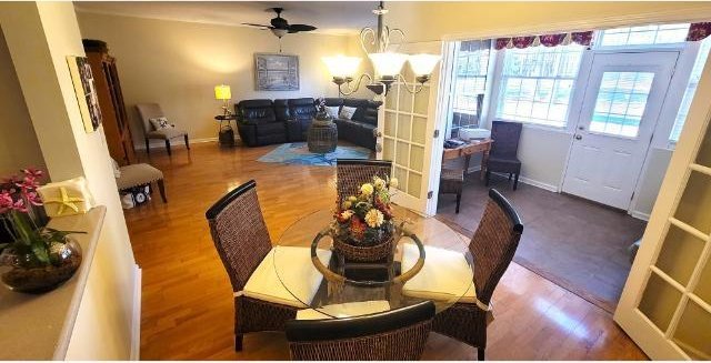 dining space with ceiling fan with notable chandelier and hardwood / wood-style flooring