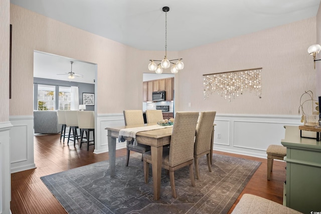 dining room featuring ceiling fan with notable chandelier, dark wood-style flooring, wallpapered walls, and a wainscoted wall