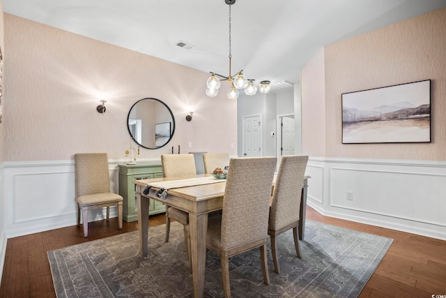 dining room featuring dark wood-style flooring, an inviting chandelier, a wainscoted wall, visible vents, and a decorative wall