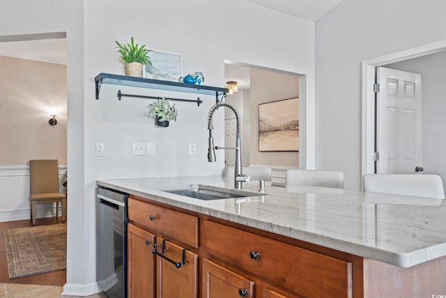kitchen featuring light wood-style flooring, light stone counters, dishwasher, a sink, and brown cabinets