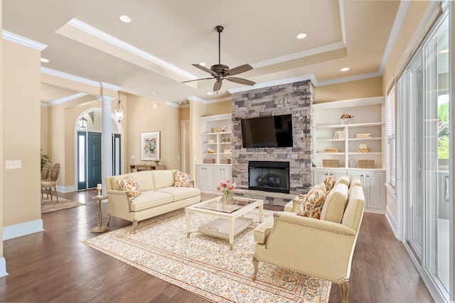 living room featuring a raised ceiling, ceiling fan, wood-type flooring, built in features, and a stone fireplace