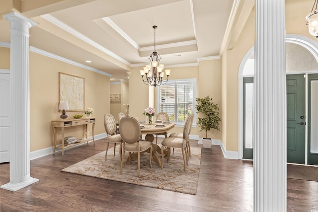 dining room with a raised ceiling, crown molding, dark hardwood / wood-style floors, ornate columns, and a chandelier