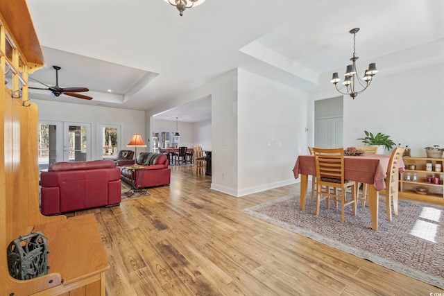 dining room featuring ceiling fan with notable chandelier, a tray ceiling, wood finished floors, and baseboards