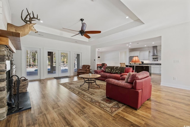 living area featuring a tray ceiling, french doors, a fireplace, and light wood finished floors