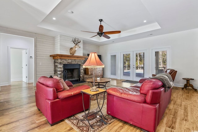 living area with light wood finished floors, baseboards, a raised ceiling, french doors, and a stone fireplace