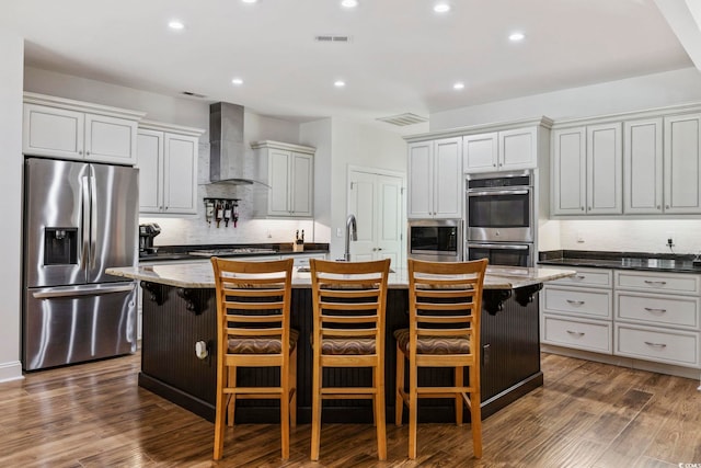 kitchen featuring appliances with stainless steel finishes, a breakfast bar area, a center island with sink, and wall chimney exhaust hood