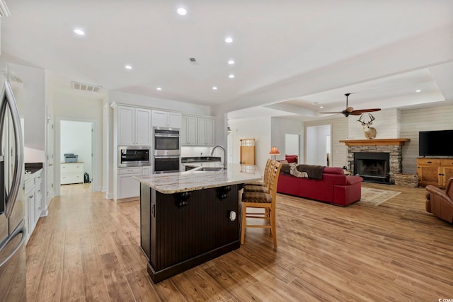 kitchen featuring a breakfast bar area, stainless steel appliances, a spacious island, white cabinets, and light stone countertops