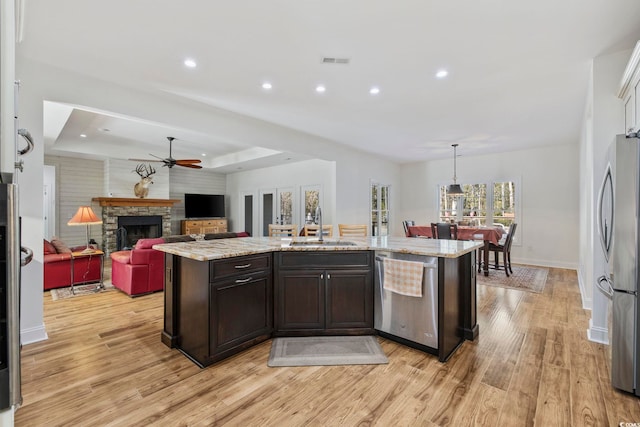 kitchen featuring open floor plan, stainless steel appliances, a center island with sink, and dark brown cabinetry