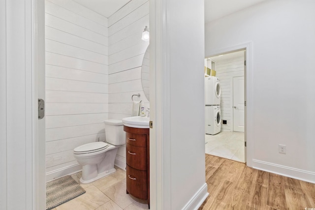 half bath featuring baseboards, stacked washer / dryer, toilet, wood finished floors, and vanity