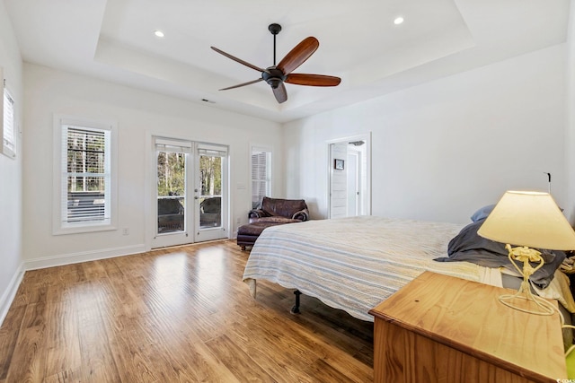 bedroom featuring wood finished floors, french doors, a raised ceiling, and access to exterior