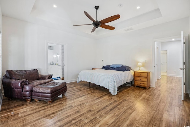 bedroom with a raised ceiling, visible vents, baseboards, and wood finished floors