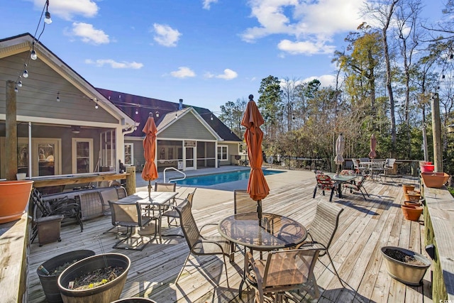 wooden terrace featuring a sunroom, outdoor dining area, and a fenced in pool