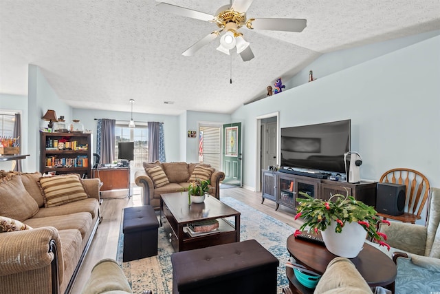 living room with ceiling fan, lofted ceiling, a textured ceiling, and light hardwood / wood-style flooring