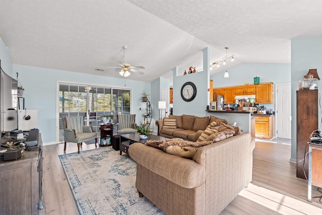 living room with a textured ceiling, light wood-type flooring, ceiling fan, and lofted ceiling