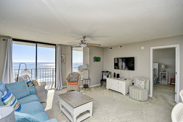 carpeted living room featuring expansive windows, ceiling fan, a water view, and a textured ceiling