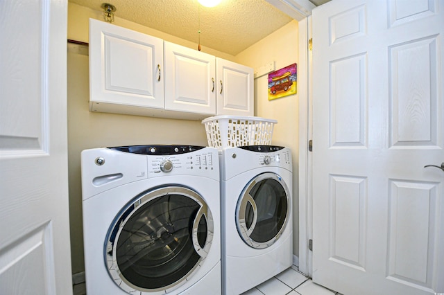 laundry room featuring light tile patterned flooring, cabinets, a textured ceiling, and washing machine and clothes dryer