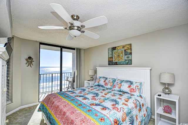 carpeted bedroom featuring ceiling fan, a wall of windows, a textured ceiling, access to outside, and a water view