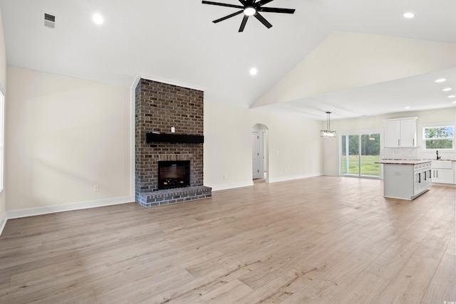 unfurnished living room featuring high vaulted ceiling, sink, ceiling fan, a fireplace, and light hardwood / wood-style floors