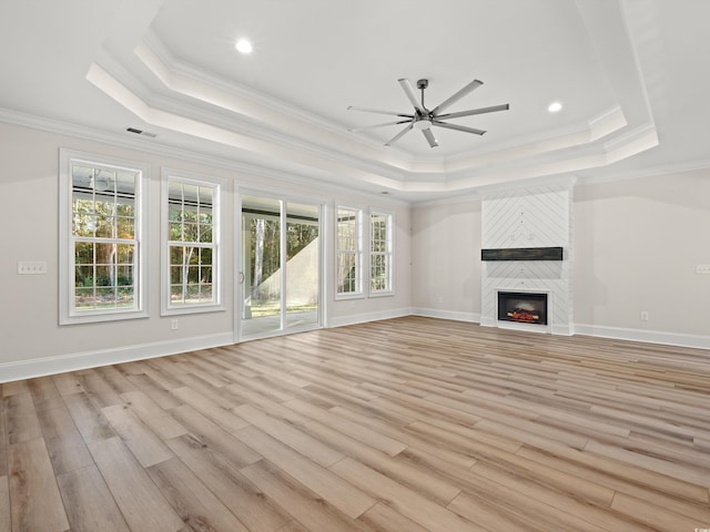 unfurnished living room with a large fireplace, ornamental molding, light hardwood / wood-style flooring, and a tray ceiling