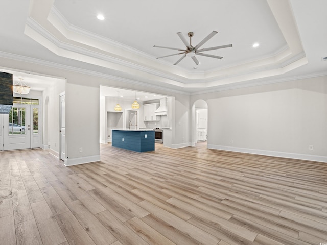 unfurnished living room featuring ceiling fan with notable chandelier, a raised ceiling, and ornamental molding