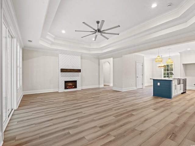 unfurnished living room featuring a raised ceiling, ceiling fan, ornamental molding, a fireplace, and light hardwood / wood-style floors