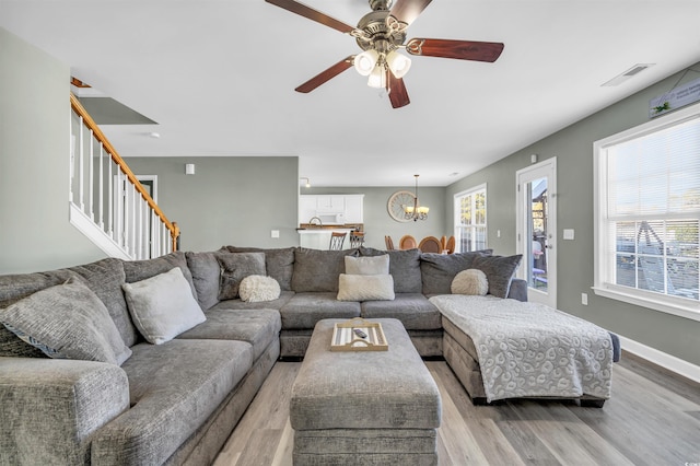 living room with light wood-type flooring and ceiling fan with notable chandelier