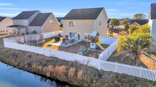 rear view of property featuring a water view, a trampoline, a patio, and a playground