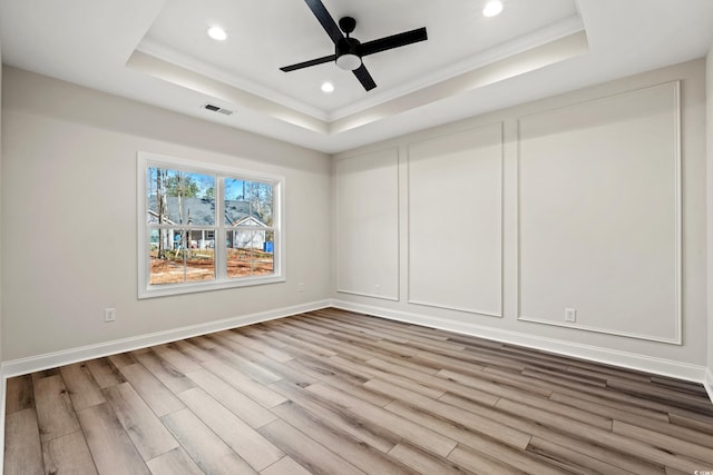 empty room with hardwood / wood-style floors, ceiling fan, and a raised ceiling