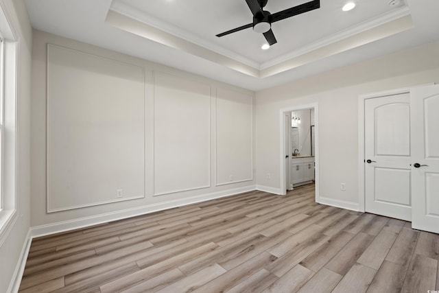 unfurnished bedroom with a tray ceiling, ensuite bath, and ceiling fan