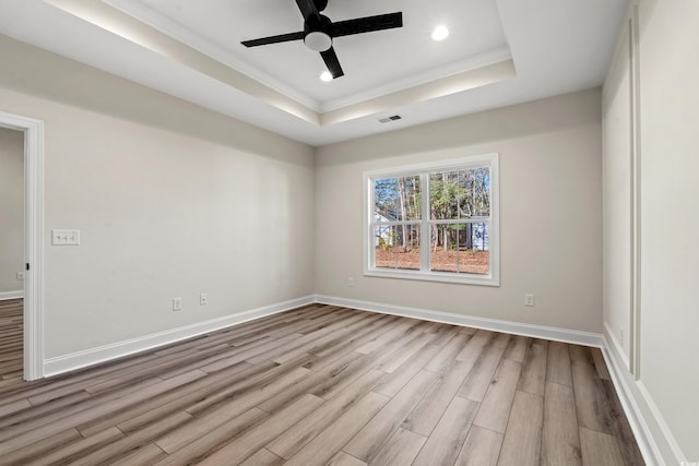 empty room featuring a raised ceiling, ceiling fan, and light hardwood / wood-style flooring