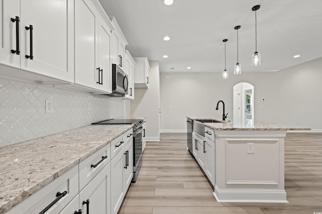 kitchen featuring light stone countertops, sink, stainless steel appliances, a center island with sink, and white cabinets