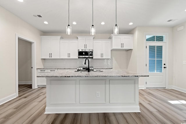 kitchen with white cabinetry, a center island with sink, and hanging light fixtures