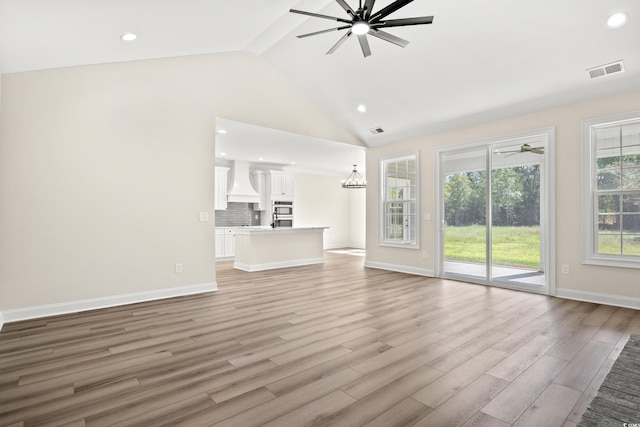 unfurnished living room with light wood-type flooring, an inviting chandelier, and vaulted ceiling