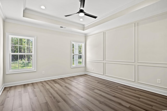 empty room with a tray ceiling, ceiling fan, wood-type flooring, and ornamental molding