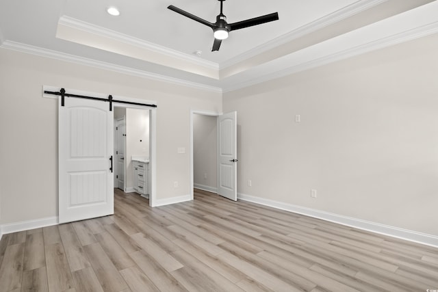 unfurnished bedroom featuring connected bathroom, ceiling fan, a raised ceiling, a barn door, and light hardwood / wood-style floors