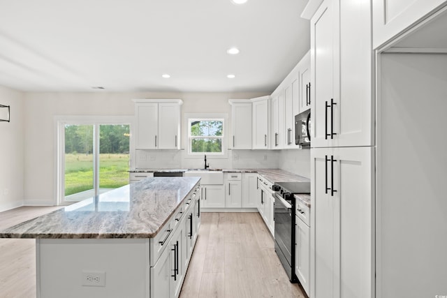 kitchen featuring light stone countertops, backsplash, a kitchen island, white cabinets, and stainless steel electric range oven