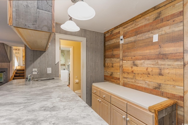 kitchen featuring sink, decorative light fixtures, washer / dryer, wooden walls, and light brown cabinetry