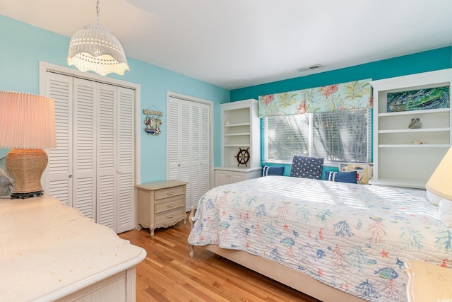 bedroom featuring an inviting chandelier, two closets, and light wood-type flooring