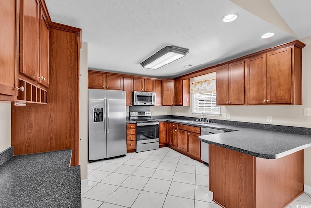 kitchen featuring appliances with stainless steel finishes, dark countertops, a sink, and a peninsula